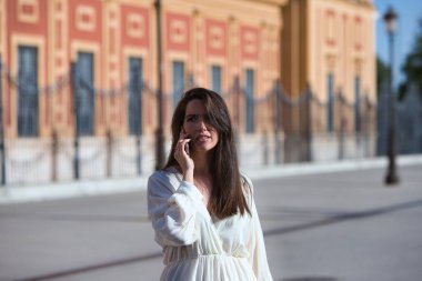 Genç ve güzel bir Latin kadın endişeli ve ciddi bir ifadeyle telefonda konuşuyor. Kadın sokakta ve şehirde yürüyor. Yeni teknoloji ve iletişim kavramı