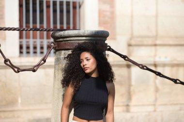 Siyah ve siyah gözlü, uzun kıvırcık saçlı, sırtına yaslanmış üzgün bir ifadeyle İspanya 'nın Sevilla katedralindeki bir sütuna yaslanan genç ve güzel bir Latin kadın. Manken fotoğraf için poz veriyor.