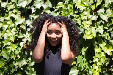 Büyük kahverengi gözleri, kıvırcık saçları ve siyah gömleği olan genç ve güzel bir Latin kadın elleri başının üzerinde umutsuzluk jesti yapıyor. Çeşitli ifadeleri kavra