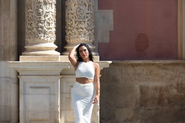 Genç İspanyol kadın, esmer ve güzel beyaz elbiseli Seville, Endülüs, İspanya 'daki tarihi bir binanın önünde. Kadın farklı vücut ifadeleri kullanıyor.