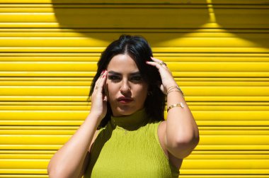 Genç İspanyol kadın, esmer ve güzel sarı arka planda yeşil elbiseli saçına ve yüzüne dokunuyor ve kameraya cüretkar ve utanmaz bir şekilde bakıyor. Güzellik ve moda konsepti