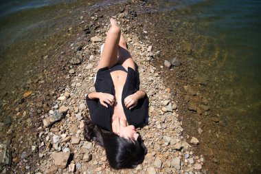 Güzel, esmer, kırmızı dudaklı, siyah gömlekli, siyah bikinili, gölde güneşlenen bir kadın. Kadın tatilinin tadını çıkarıyor. Fotoğraf yukarıdan çekildi