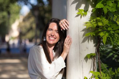 Genç ve güzel Latin kadın parktaki beyaz mermer bir sütuna yaslanıyor. Kadın mutlu ve gülümsüyor Seville, İspanya 'da güneşli bir günde.