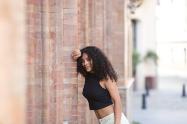 Siyah gözlü, uzun kıvırcık saçlı, güzel bir Latin kadın kafasını tuğla duvara yaslamış bir kola yaslıyor. Kadın İspanya, Seville 'de tatilde mutlu.