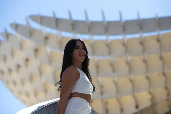 stock image Young Spanish woman, brunette and beautiful in white dress on the railing of the stairs of the square of the mushrooms in Seville, andalusia, Spain. The woman is relaxed and enjoying in the city