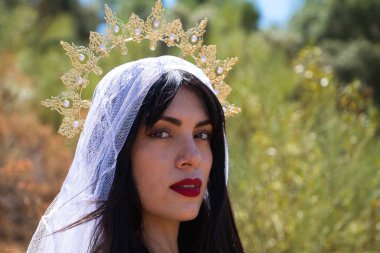 Güzel, genç, esmer, kırmızı dudaklı, beyaz duvak takmış, altın bir taç takmış bakire Meryem ya da tanrıça. Kadın sanki bir hayaletmiş gibi bitkilerle dolu bir ormanda.