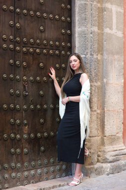 Sevilla 'lı güzel bir İspanyol kadın zarif siyah bir elbise ve ipek çiçeklerle işlenmiş tipik bej ipek bir şal giyiyor. Şal Endülüs 'e ait ve flamenko havası var.