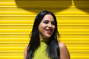 Genç İspanyol kadın, esmer ve güzel sarı arka planda yeşil elbisesi var gülümsüyor ve çok mutlu. 20 Haziran, yılın en mutlu günü. Mutluluk ve neşe kavramı