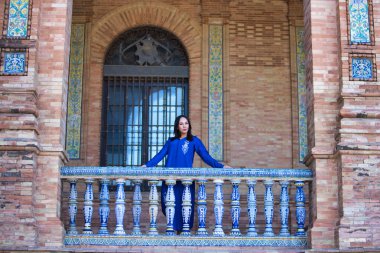 Genç ve güzel Faslı kadın, esmer, abaya gibi giyinmiş, tipik Fas kostümü giymiş, İspanya 'nın Seville meydanının fayanslı ve tuğlalı balkonuna bakıyor. Kadın ciddi.