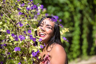 Koyu, genç ve güzel bir kadın, mor çiçeklerin arasında güneşleniyor, kadın sakin ve gözlerini kapatıyor, mutlu ve gülümsüyor.