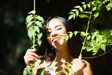 Koyu, genç ve güzel bir kadın, yeşil yapraklı bir sarmaşığın arasına gizlenmiş, ve güneş ile gölge arasında, kadın bitkiyi elinde tutuyor ve gevşemiş, mutlu ve gülümsüyor. Doğadaki mutluluk kavramı