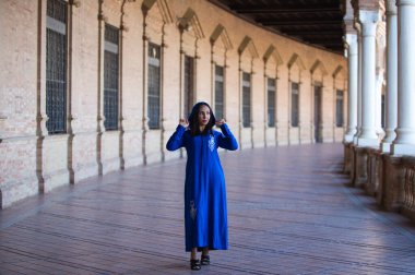 Genç, güzel, esmer Fas 'lı kadın, mavi abaya giymiş, tipik Arap kostümü giymiş, Sevilla' da İspanya meydanında kemer ve sütunlar arasında yürüyor. Afrikalı kadın Avrupa 'da tatilde.