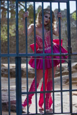 Pembe giyinmiş tuhaf sarışın travesti parmaklıklar ardında. Travesti kadın dehşete kapılır, çığlık atar ve üzülür, şok olur ve şaşkına döner. lgbtiq hakları ve eşitliği kavramı.