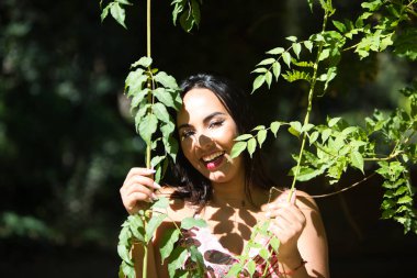 Koyu, genç ve güzel bir kadın, yeşil yapraklı bir sarmaşığın arasına gizlenmiş, ve güneş ile gölge arasında, kadın bitkiyi elinde tutuyor ve gevşemiş, mutlu ve gülümsüyor. Doğadaki mutluluk kavramı