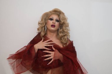Sarı peruklu, lüks küpeli ve beyaz arka planda kırmızı ipekle kaplanmış bir travesti Bakire Meryem 'i taklit ediyor. lgtbqi hakları ve eşitliği kavramı