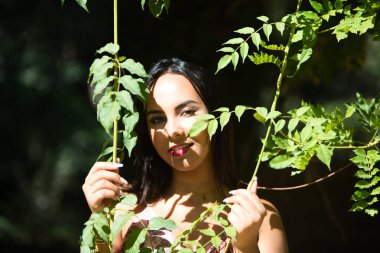 Koyu, genç ve güzel bir kadın, yeşil yapraklı bir sarmaşığın arasına gizlenmiş, ve güneş ile gölge arasında, kadın bitkiyi elinde tutuyor ve gevşemiş, mutlu ve gülümsüyor. Doğadaki mutluluk kavramı