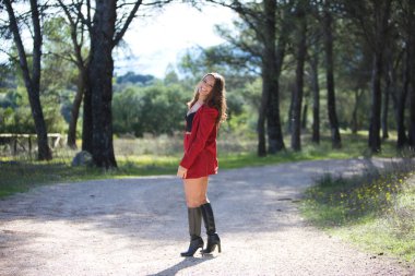 Güzel esmer Latin kadın parkta ağaçların arasında yürürken farklı yüz ve vücut hareketleri yapıyor ve eğleniyor. Fotoğraf arkadan çekilmiş.