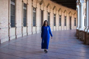 Genç, güzel, esmer Fas 'lı kadın, mavi abaya giymiş, tipik Arap kostümü giymiş, Sevilla' da İspanya meydanında kemer ve sütunlar arasında yürüyor. Afrikalı kadın Avrupa 'da tatilde.