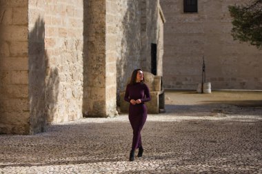 İspanya 'nın Seville kentindeki bir köyde, bir manastırın yanındaki kaldırım taşından bir sokakta poz veren zarif mor elbiseli güzel bir genç kadın. Kadın farklı ifadeler ve jestler yapıyor.