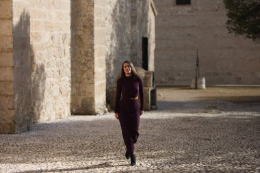 İspanya 'nın Seville kentindeki bir köyde, bir manastırın yanındaki kaldırım taşından bir sokakta poz veren zarif mor elbiseli güzel bir genç kadın. Kadın farklı ifadeler ve jestler yapıyor.