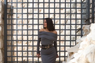 Gri giyinmiş, sırtına yaslanıp gri metal ızgaraya tutunan genç ve güzel bir kadın. Kadın mutlu ve eğleniyor. Mutluluk ve pozitifliği kavra.