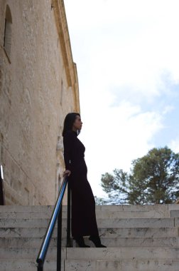 Genç ve güzel bir kadın zarif bir menekşe elbise giyip merdivenlere yaslanmış, farklı yerlere bakıyor. Depresyonda ve üzgün olduğu için. Ruh sağlığı konsepti.