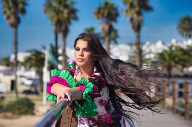 Latin bir kadın, genç ve güzel dans eden flamenko saçları havada elini ve kolunu korkuluklara uzatıyor. Dalgalı ve çiçekli beyaz elbiseli kadın tipik Endülüs.