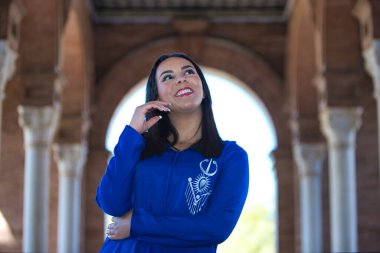 Fas 'lı kadın portresi, esmer, genç ve güzel, abaya ile giyinmiş, tipik Fas kostümü farklı ifadeler sergiliyor, Sevilla meydanındaki beyaz mermer sütunlar arasında yer almaktadır.