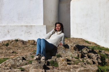 Genç ve güzel Latin esmer kadın huelva, Endülüs 'teki Cortegana Kalesi' nin çevresinde gelişigüzel giyinmiş ve büyük bir taşın üzerinde oturuyor.