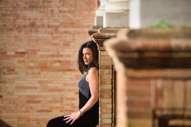 Siyah elbiseli genç ve güzel esmer kadın Sevilla, Endülüs 'teki İspanya' nın ünlü meydanında. Kadın sırtını mermer bir sütuna yaslıyor ve ileriye bakıyor.