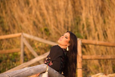 İspanyol kadın, esmer ve tipik flamenko dans kostümü giymiş güzel flamenko dansçısı saçları havada, ahşap korkulukta. Altın saat fotoğraf oturumu