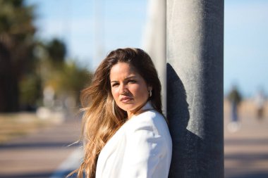 Genç ve güzel sarışın bir kadının portresi sokak lambasına yaslanmış ve kameraya bakıyor, kadın ciddi ve beyaz bir ceket giyiyor.