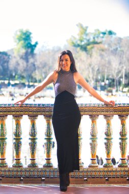 Esmer kadın, Endülüs, Seville 'deki ünlü İspanyol meydanında seramik balkonda genç ve güzel. Arka planda ağaçlar ve bahçeler var. Kız mutlu ve gülümsüyor.