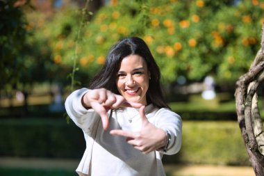 Genç ve güzel Latin esmer kadın parmaklarıyla kameraya bakıp gülümsüyor. Yüzü odak ve elleri bulanık