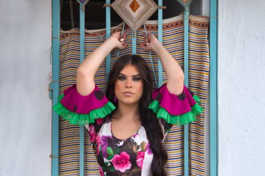 Genç ve güzel bir kadın elleriyle demir bir çite yaslanmış flamenko dansı yapıyor. Çiçeklerle dolu tipik bir Endülüs sokağında. Üzerinde fırfırlı ve çiçekli kuyruklu bir elbise var.