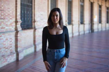 Esmer bir kadın, kot pantolon giymiş genç ve güzel ve siyah bir elbise giymiş Seville, Endülüs 'teki İspanya' nın ünlü meydanında yürüyor. Kadınlar anıtın tadını çıkarıyor.