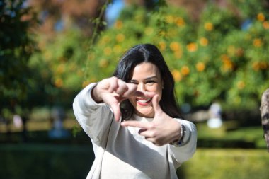 Genç ve güzel Latin esmer kadın parmaklarıyla kameraya bakıp gülümsüyor. Yüzü odak ve elleri bulanık