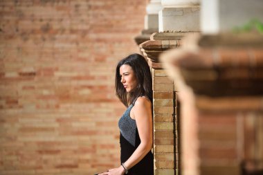 Siyah elbiseli genç ve güzel esmer kadın Sevilla, Endülüs 'teki İspanya' nın ünlü meydanında. Kadın sırtını mermer bir sütuna yaslıyor ve ileriye bakıyor.