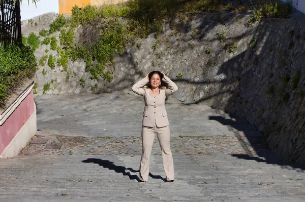 Genç ve güzel sarışın kadın bir caddenin merdivenlerinden yukarı çıkıyor. Kadın bej bir ceket giyiyor. Kadın mutlu ve farklı vücut duruşları sergiliyor. Fotoğraf yukarıdan çekildi