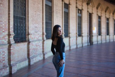 Esmer bir kadın, kot pantolon giymiş genç ve güzel ve siyah bir elbise giymiş Seville, Endülüs 'teki İspanya' nın ünlü meydanında yürüyor. Kadınlar anıtın tadını çıkarıyor.