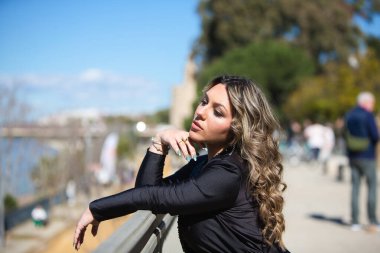 Siyah giyinmiş genç, güzel sarışın kadın gri metal korkuluklara yaslanıyor. Kadın bir elinde dinleniyor. İlginç görünüyor.