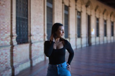 Esmer bir kadın, kot pantolon giymiş genç ve güzel ve siyah bir elbise giymiş Seville, Endülüs 'teki İspanya' nın ünlü meydanında yürüyor. Kadınlar anıtın tadını çıkarıyor.