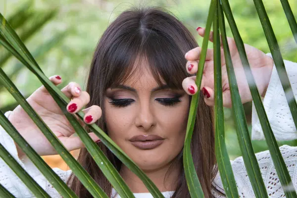 Güzel, genç esmer kadın elinde bir palmiye yaprağı tutuyor ve ona bakıyor. Kadın, İspanyol bir kadının büyük siyah gözleriyle çok anlamlı. Güzellik ve moda