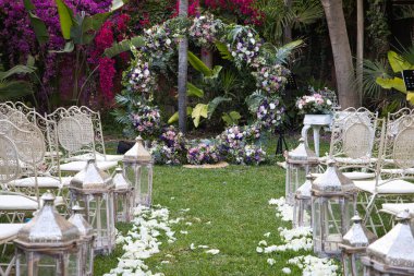 Açık hava düğününde koridorda yürüyüşün görüntüsü çok güzel. Arka planda, misafirler, gelinler ve damatlar için çiçek ve sandalyelerin olduğu bir fotoğraf.