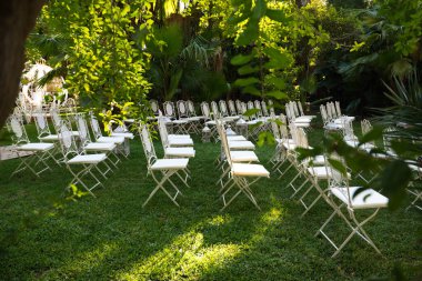 Dışarıdaki bir düğün töreninde misafirleri oturtmak için çimlere beyaz sandalyeler.