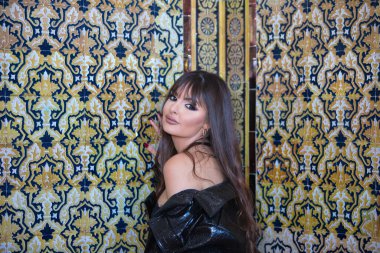 Genç ve güzel esmer, üst ve deri ceketli kadın kamerayı baştan çıkarmak için oynuyor. Arka planda Seville 'de bir duvarda Arap tarzı fayanslar var.