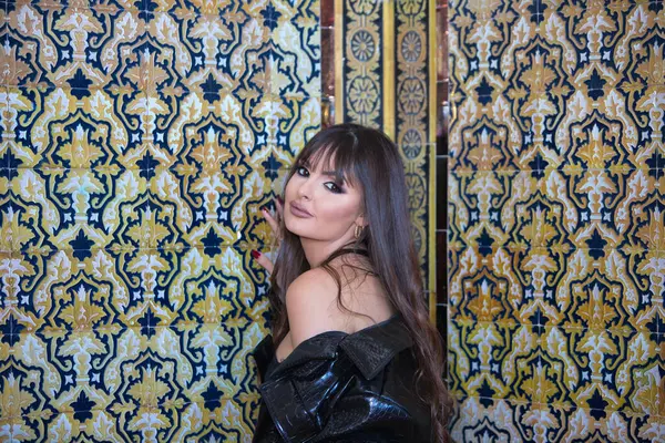 Genç ve güzel esmer, üst ve deri ceketli kadın kamerayı baştan çıkarmak için oynuyor. Arka planda Seville 'de bir duvarda Arap tarzı fayanslar var.