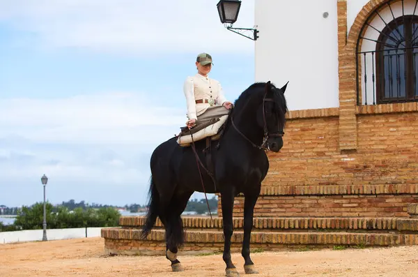 İspanya 'nın Endülüs şehrinde düzenlenen popüler festivalde safkan bir İspanyol siyah atına binen genç ve güzel bir kadın. Kadın tipik bir atlı kadın kostümü giyiyor. Arka planda inziva yeri var.