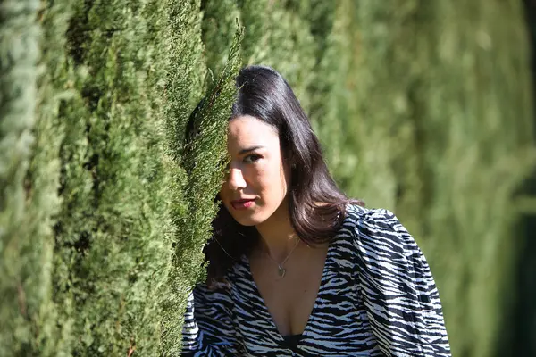 Yolu ayıran yeşil çitlerin arkasında saklanan genç ve güzel Latin esmer bir kadının portresi.