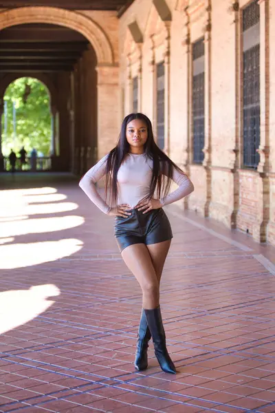 Deri şort, siyah çizme ve bej bluz giyen genç ve güzel Afrikalı kadın tatilde ve İspanya 'nın ünlü meydanında Seville' de yürüyor. Seyahat ve tatil konsepti